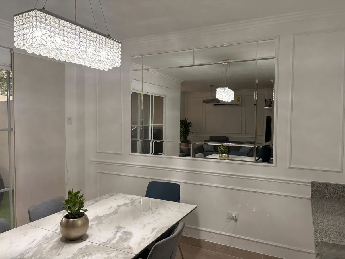 Pared espejada en un comedor, reflejando la lámpara de cristal y la mesa de mármol