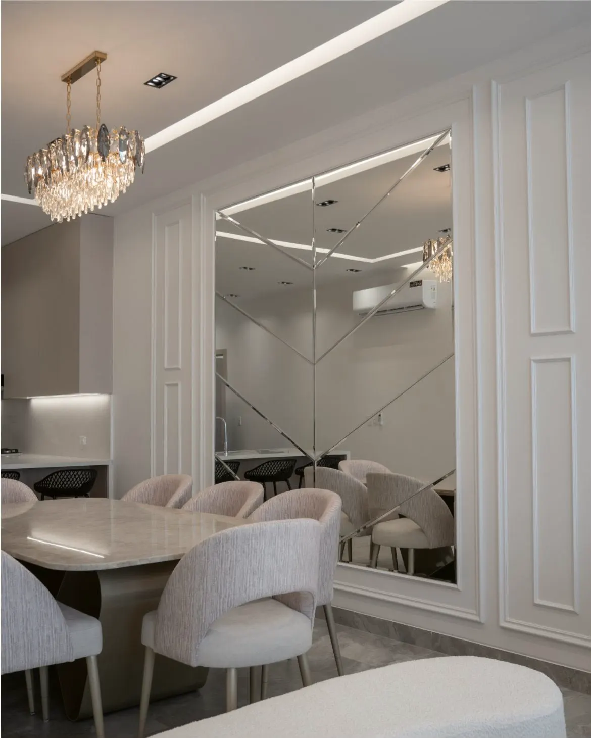 Pared espejada en un comedor con molduras blancas y lámpara de cristal